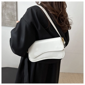 Detail of a minimalist white patent leather shoulder bag with irregular flap design