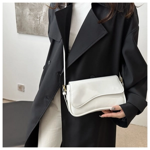 Close-up of white patent leather shoulder bag with a curved flap and gold metal hardware
