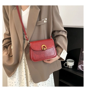 Detail of red glossy leather shoulder bag with gold horseshoe buckle on model style