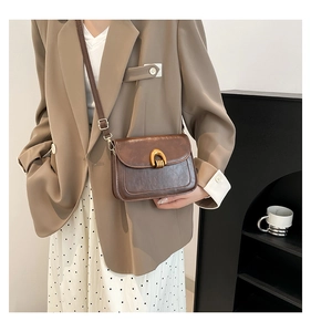 Detail of vintage brown saddle bag featuring a gold U-shaped buckle and textured leather