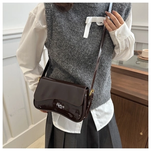 Detail of dark brown patent leather crossbody bag with glossy finish and gold hardware