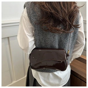 Detail view of burgundy patent leather crossbody bag with adjustable gold buckle strap