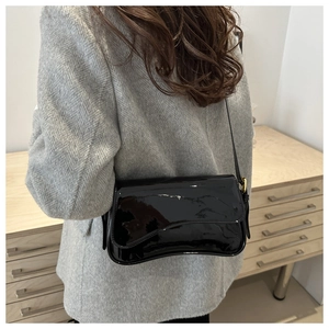 Detail of glossy black patent leather shoulder bag with gold hardware on a model