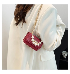 Détail du mini sac rouge effet croco avec poignée en perles et chaîne dorée sur costume