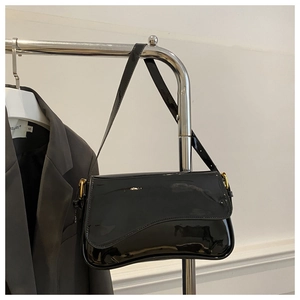 Détail du sac bandoulière en cuir verni noir brillant avec boucle dorée sur veste