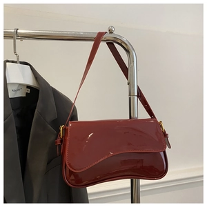 Détail du sac à bandoulière en cuir verni bordeaux avec boucle dorée et rabat incurvé