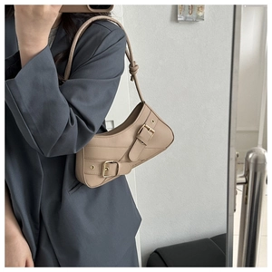 Détails d'un sac selle beige avec deux lanières à boucles et silhouette demi-lune chic