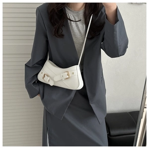 Détail du sac demi-lune blanc avec boucles dorées porté sur une veste de costume grise