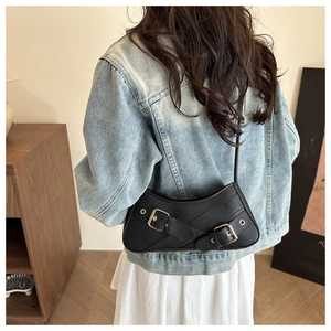 Vue latérale d'un sac sous les bras vintage en cuir noir avec boucles dorées sur denim