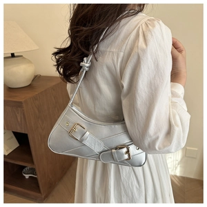 Détail du sac argenté métallisé avec boucles décoratives sur robe blanche plissée