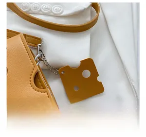 Detail of ginger leather mini bag with a creative cheese-shaped charm on a white blazer