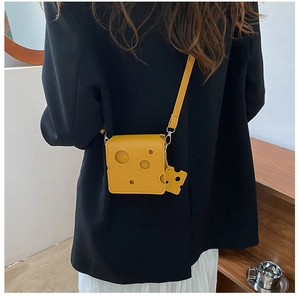 Close-up of a yellow cheese-shaped mini crossbody bag worn with a black blazer