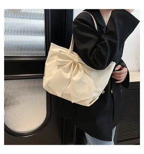Gros plan d'un sac cabas blanc crème avec un grand nœud décoratif et texture en cuir PU souple