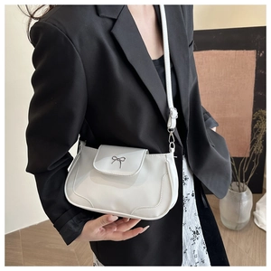Close-up of white leather saddle bag featuring a silver metal bow accent and shoulder strap