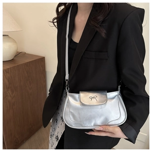 Detail of silver shoulder bag with metallic bow buckle shown on a model