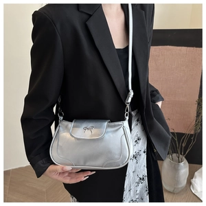 Detail of silver matte shoulder bag featuring a minimalist metal bow on the front flap