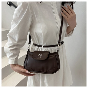 Macro detail of silver metal bow buckle on dark brown retro leather crossbody bag