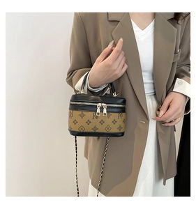 Detail of a cylinder handbag with NY print, gold hardware chain, and leather top handle