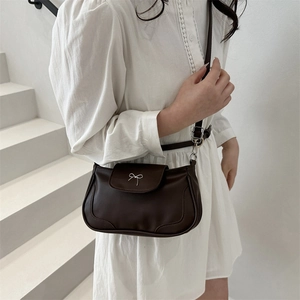 Dark brown matte saddle bag with silver bow accent shown in a minimalist studio setting