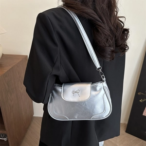 Silver metallic saddle bag with bow detail worn by model in a minimalist home setting