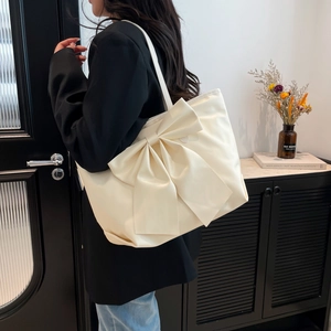 Grand sac cabas beige crème avec nœud élégant porté par un mannequin dans un décor moderne