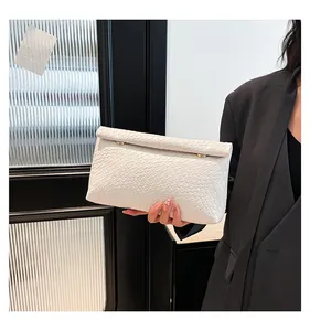 Détail de pochette tressée blanche avec garnitures dorées et fermeture à rabat