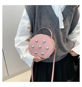 Detail of pink round crossbody bag with silver rivets and top handle worn by a model