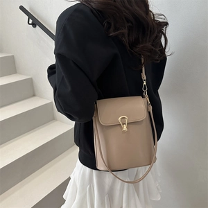 Sac seau beige minimaliste avec fermoir goutte d'or porté par un mannequin avec style
