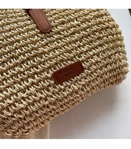 Close-up of woven straw bag detail featuring brown leather strap and brand name tag