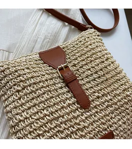 Detail of white straw crossbody bag with brown leather strap and gold buckle closure