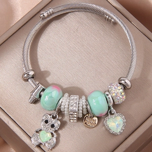 Zilveren armband met groene hart- en beerbedeltjes op champagnekleurig satijn