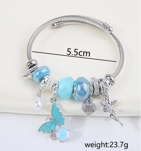 Detail of silver bracelet featuring blue butterfly charm and heart-shaped FOR KEEPS pendant