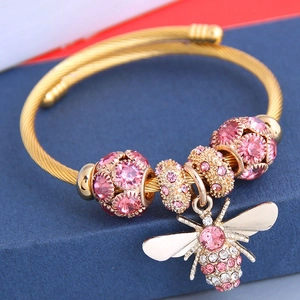 Gros plan d'un bracelet doré avec des perles en cristal rose et un pendentif abeille brillant