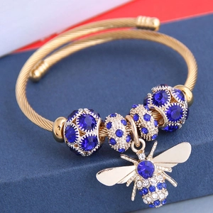 Détail d'un bracelet doré torsadé avec breloque abeille et perles bleues sur support