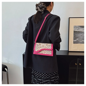 Detail of fuchsia embossed crossbody bag styled with a black suit and polka dot dress