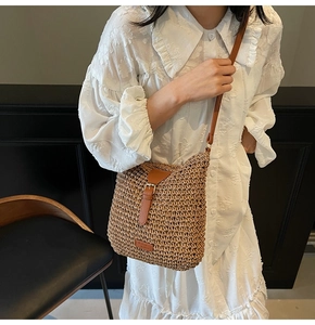 Detail of straw woven crossbody bag with brown leather strap and embossed label