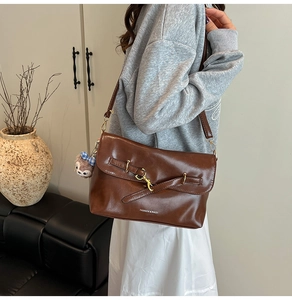 Dettaglio di una borsa quadrata in vernice marrone con tracolla regolabile e fibbia in metallo