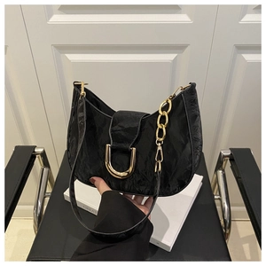 Close-up of black crescent shoulder bag featuring gold U-shaped buckle and chunky chain link