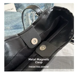Detail of silver magnetic snap closure on a black synthetic leather tote bag