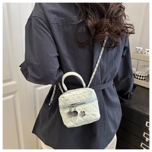 Detail of quilted mini bucket bag featuring a chain strap and floral charm accessory