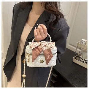 Detail of white quilted vanity bag with golden flower charm and silk scarf handle