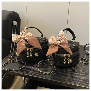 Detail of black quilted mini bag with gold floral charm and silk scarf handle detail