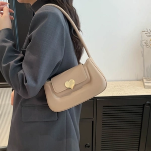 Minimalist beige underarm bag with gold heart buckle shown on model in a modern room