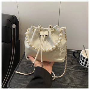 Close-up of beige satin bucket bag with floral embroidery and elegant pearl handle