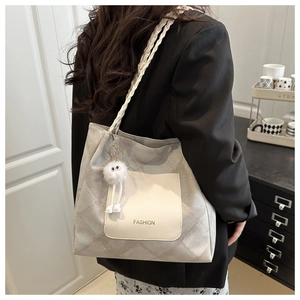 Detail of grey quilted tote bag with woven strap and plush charm worn by a model