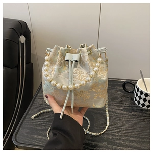 Detail of light blue bucket bag with gold embroidery and white pearl handle