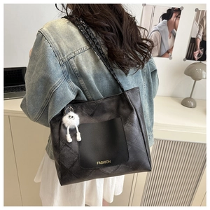 Detail of black quilted tote bag with woven shoulder strap and plush monster charm