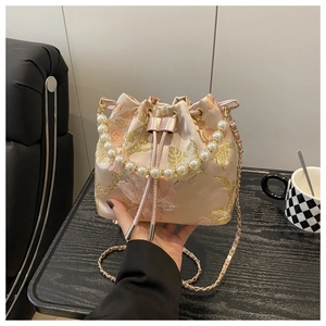 Detail of floral embroidery on satin bucket bag with pearl handle and golden chain