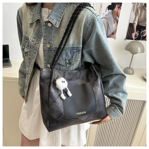 Detail view of black tote bag featuring woven straps and a plush monster charm