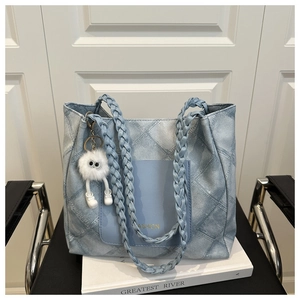 Detail of light blue denim tote bag featuring braided handle and plush monster charm